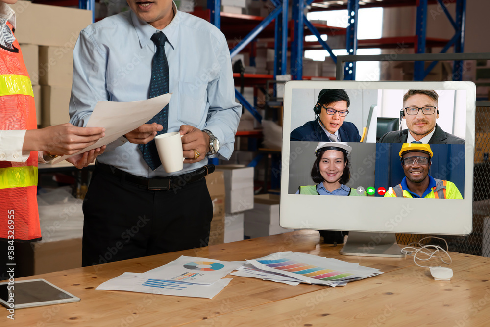 Warehouse staff talking on video call at computer screen in storage warehouse . Online software tech