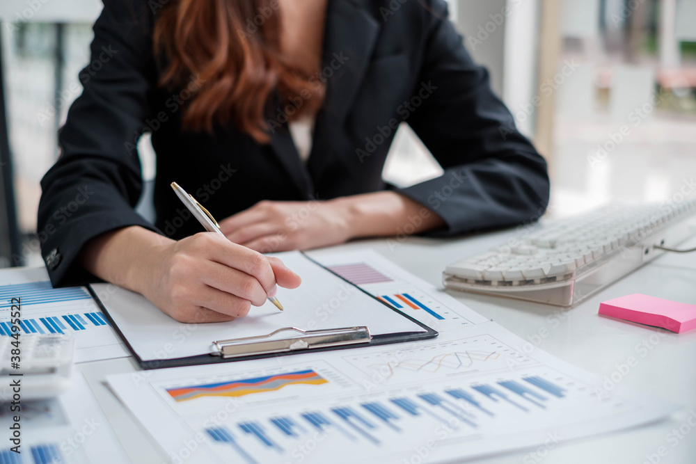 A serious business woman in a suit is reviewing and taking notes of the companys performance chart