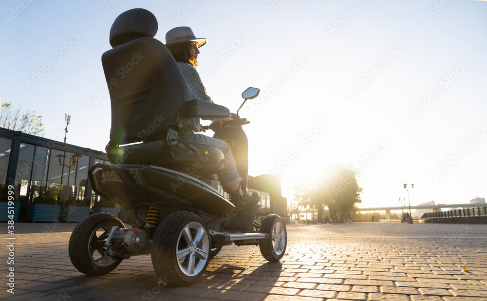 Woman tourist riding a four wheel mobility electric scooter on a city street.	