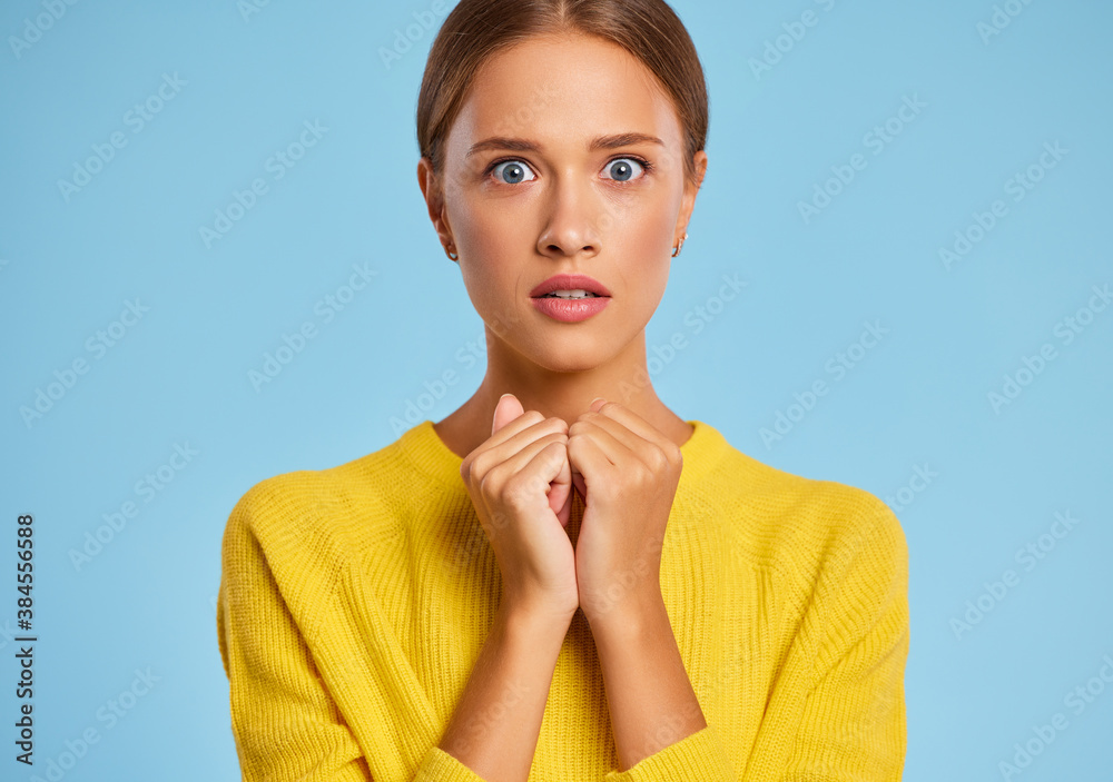 funny emotional girl in a yellow sweater with a surprised scared face on    blue background.