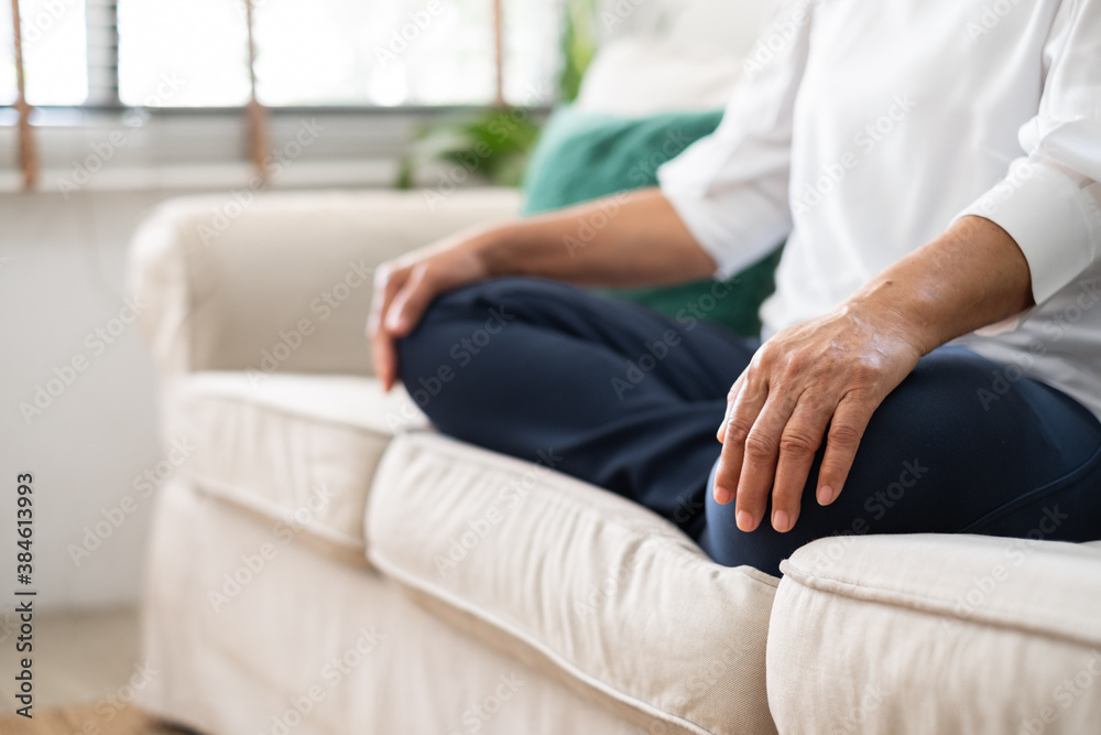 Senior old Asian woman sitting on sofa practicing yoga and meditation at home, retirement and wellbe