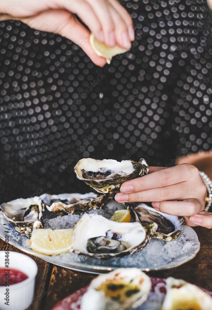 Hands of woman putting lemon juice and eating fresh Irish oysters over ice in plate in restaurant, s