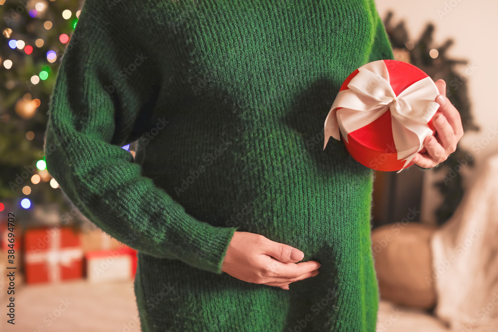 Beautiful pregnant woman with gift at home on Christmas eve, closeup