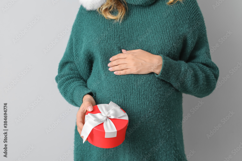 Beautiful pregnant woman with gift on light background, closeup