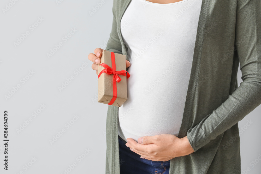 Beautiful pregnant woman with gift on light background, closeup