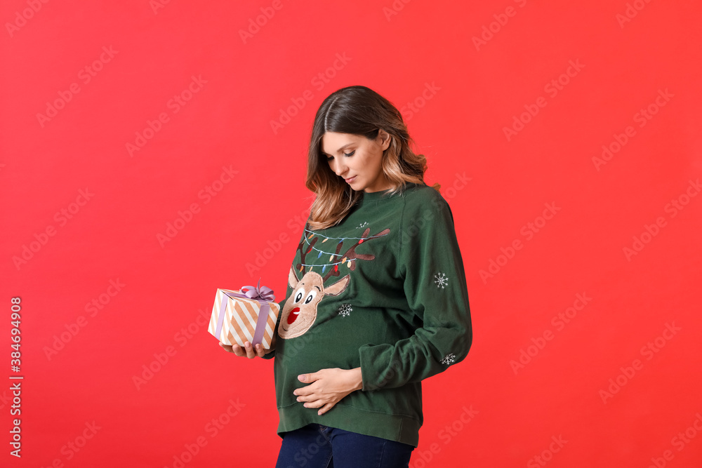 Beautiful pregnant woman with Christmas gift on color background