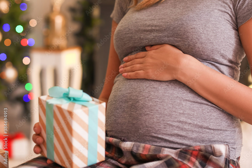 Beautiful pregnant woman with gift at home on Christmas eve, closeup