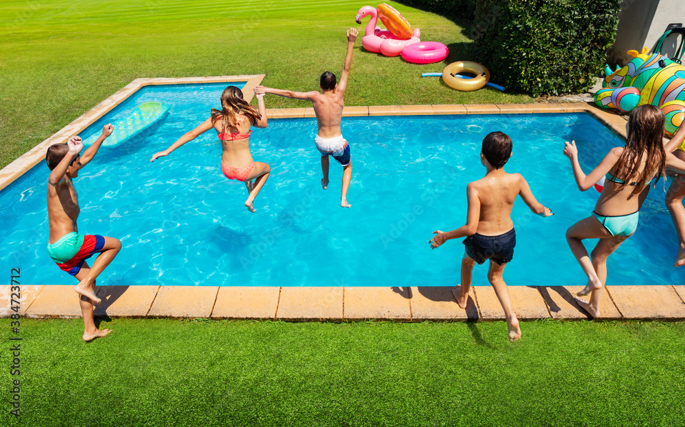 Group of young kids jump into the swimming pool about to dive view from behind and above