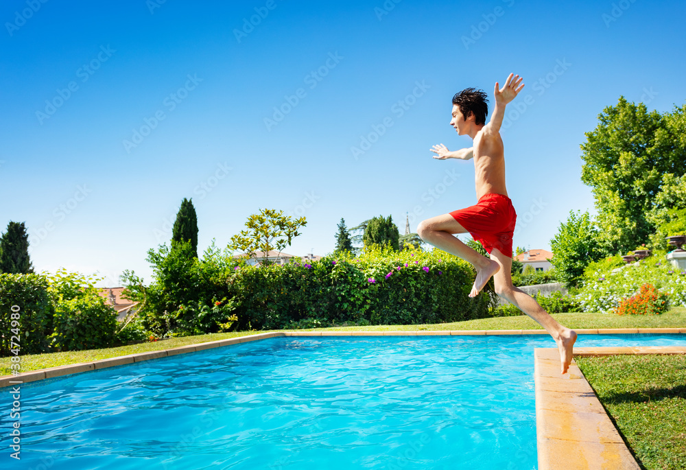 Handsome boy jump in mid air into the swimming pool water view from side with hands up