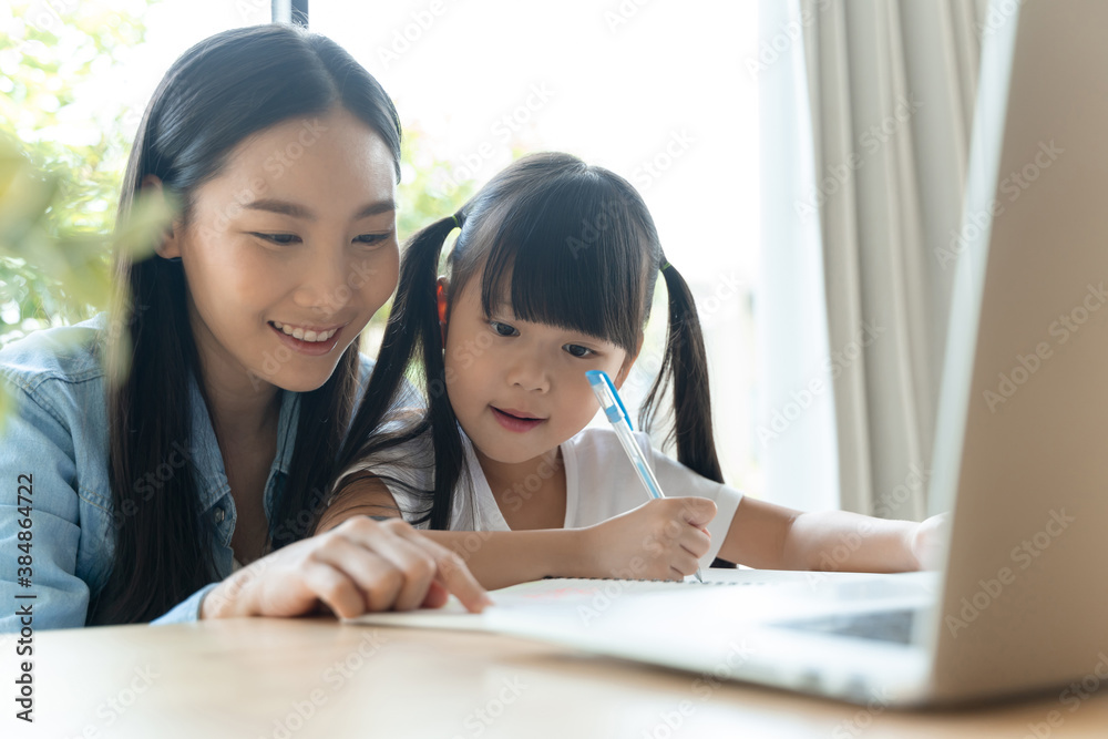 young asian mother on blue shirt enjoy teaching her adorable daughter a homework on a laptop. Asian 