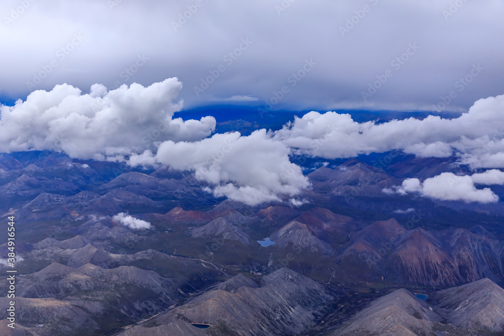 阳光明媚的日子里，云层和山峰上方的鸟瞰图。飞机上的山景。