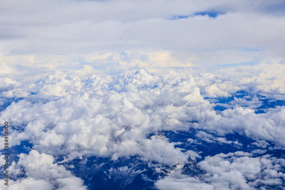 Aerial view above the clouds and mountain peaks on a sunny day.