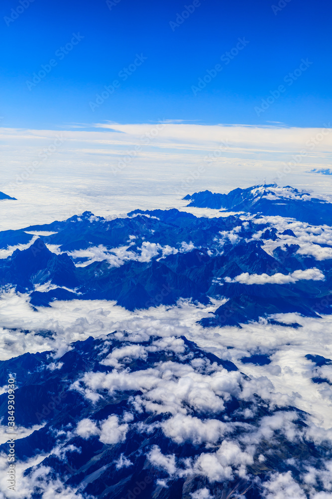 Aerial view above the clouds and mountain peaks on a sunny day.