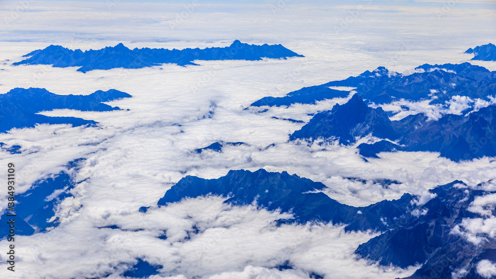 Aerial view above the clouds and mountain peaks on a sunny day.