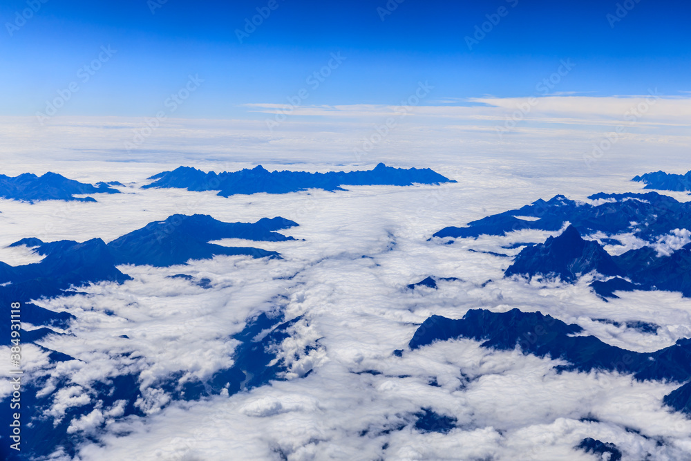 Aerial view above the clouds and mountain peaks on a sunny day.