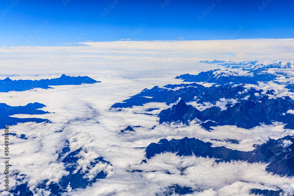 Aerial view above the clouds and mountain peaks on a sunny day.