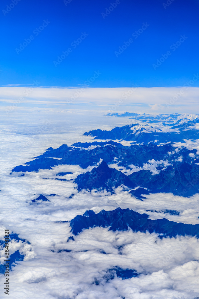 Aerial view above the clouds and mountain peaks on a sunny day.