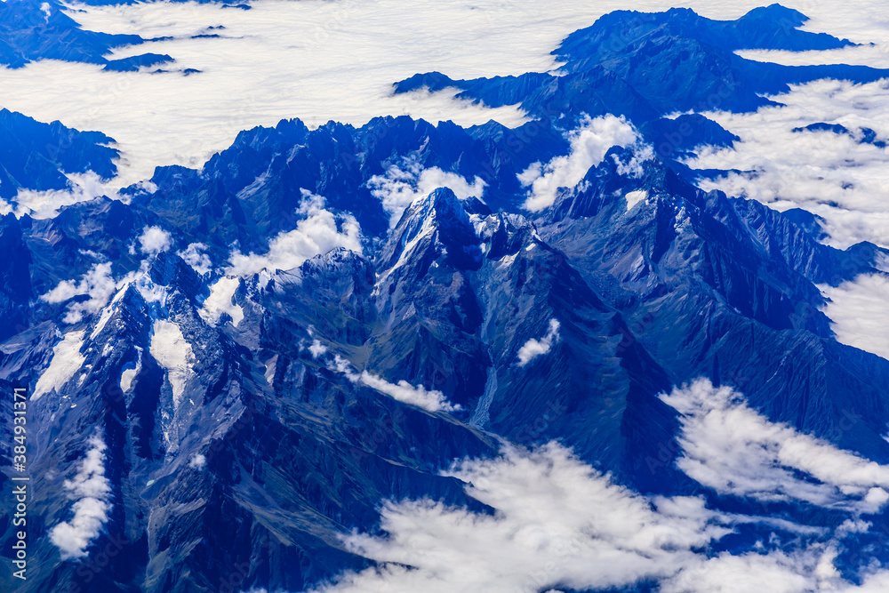 Aerial view above the clouds and mountain peaks on a sunny day.