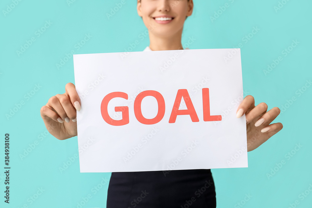 Young businesswoman holding paper with word GOAL on color background