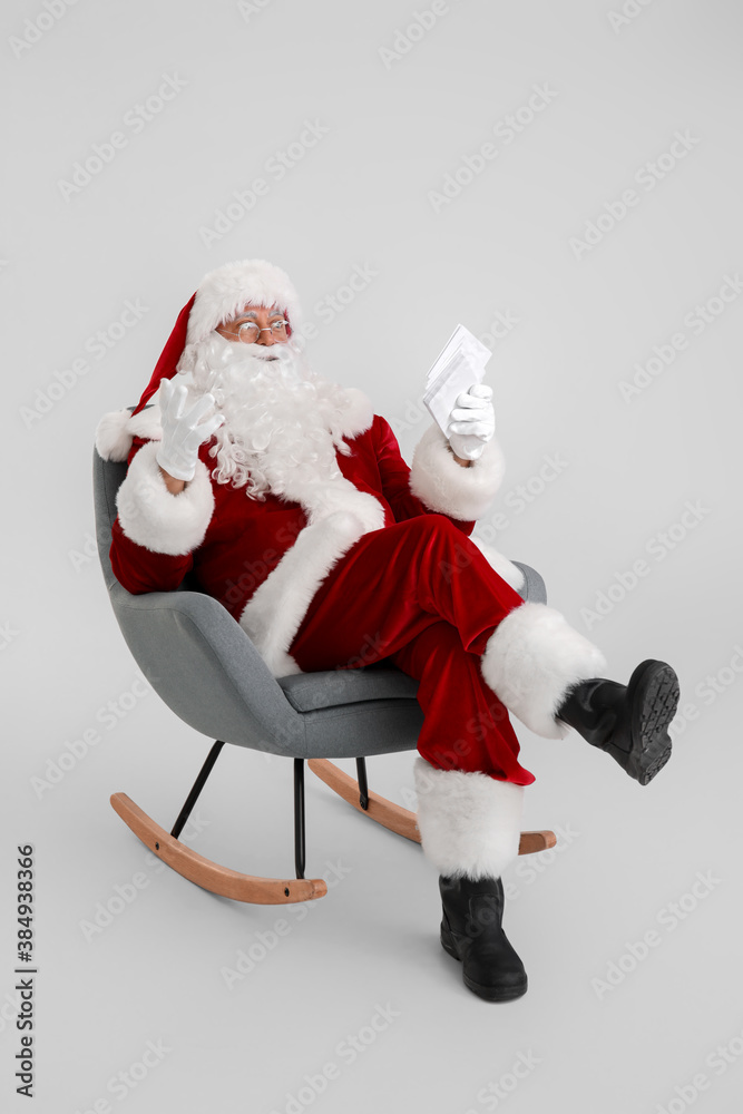 Santa Claus with letters sitting in armchair on light background