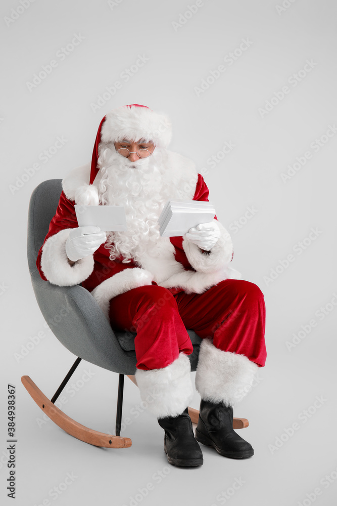 Santa Claus with letters sitting in armchair on light background