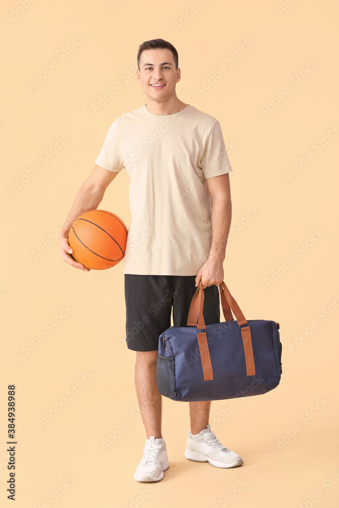 Sporty young man with bag and ball on color background