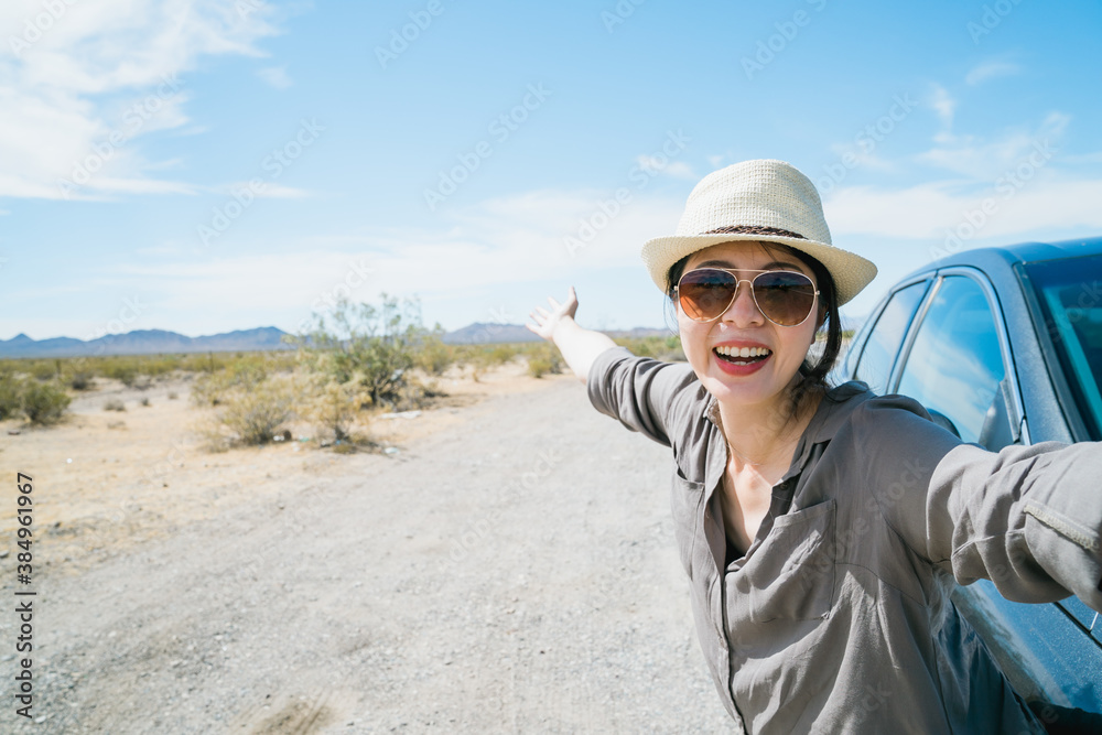 asian woman by car having jolly laugh is taking selfie with wild nature in desert region. female vis