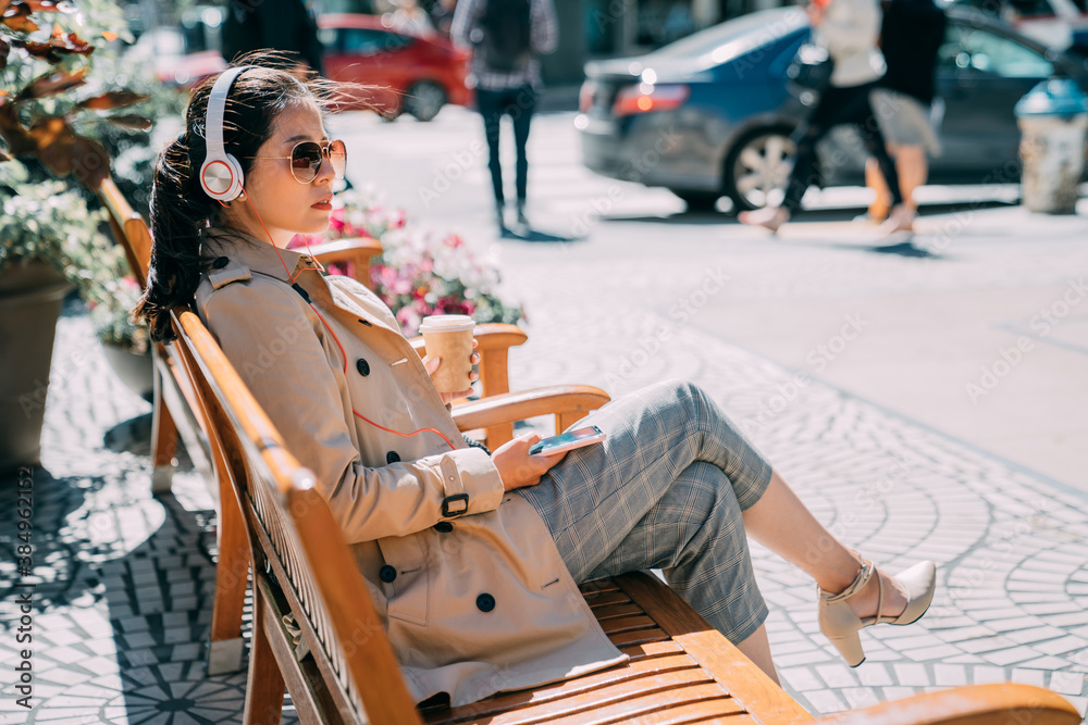 confident asian chinese woman in sunglasses listening to music from smartphone with headphones in ci