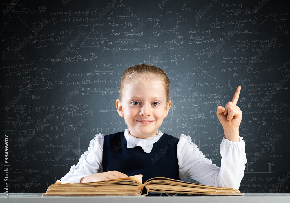 Smiling little girl sitting at desk with open book