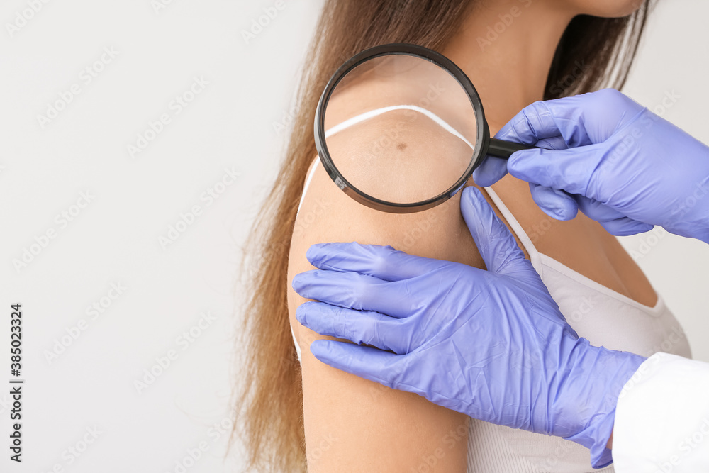 Dermatologist examining patient on light background