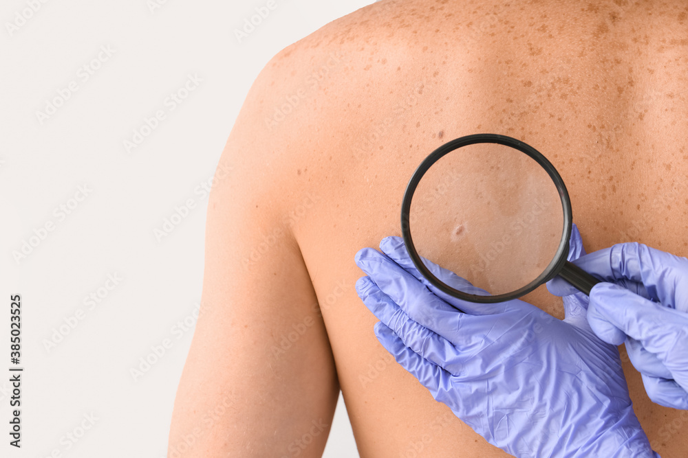 Dermatologist examining patient on light background