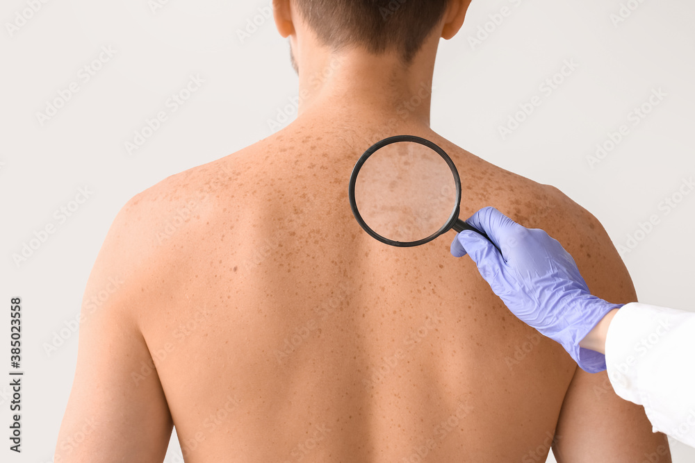 Dermatologist examining patient on light background