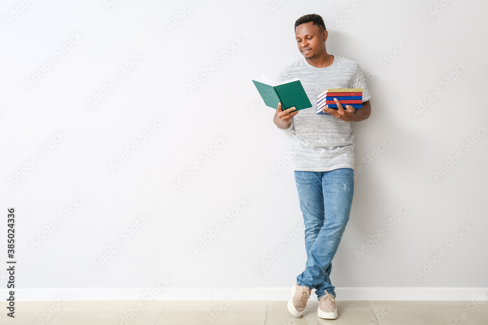 African-American man with books near light wall