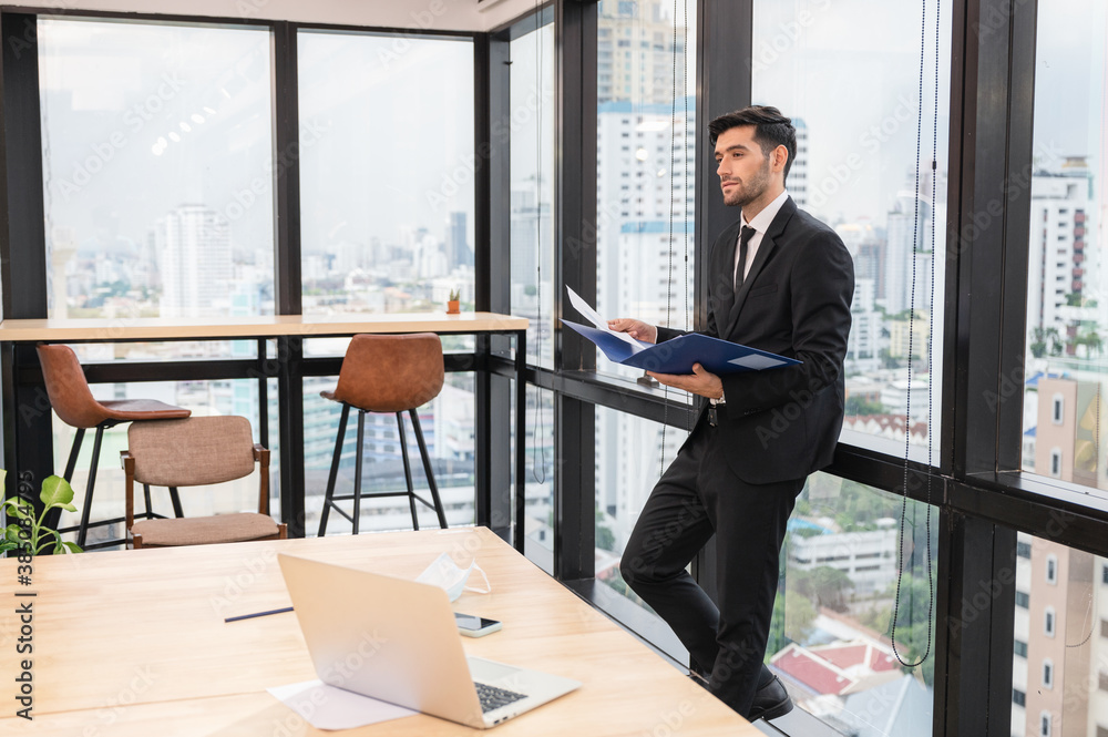 Young caucasian businessman holding financial document and looking in modern office