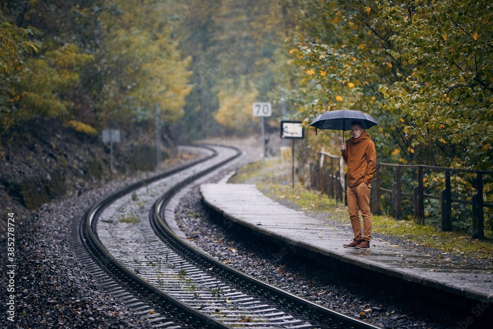 Man with umbrella during rain waiting at railroad station