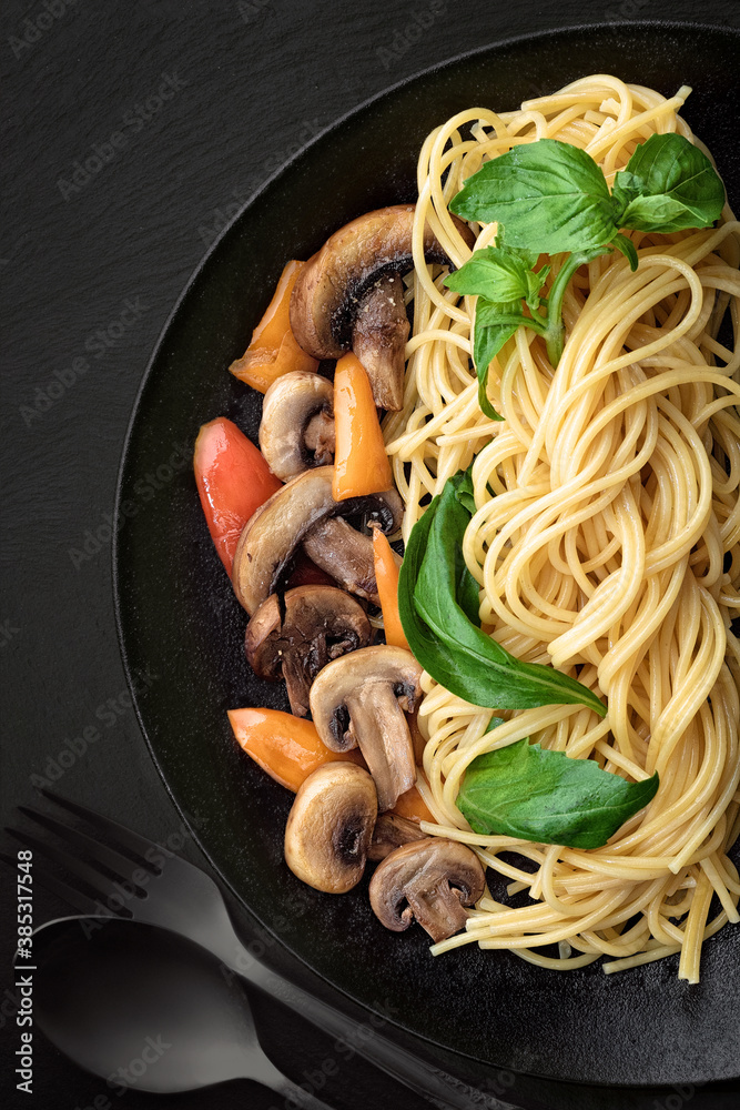 Pasta spaghetti with mushrooms and vegetables on black plate. Menu concept.Top view.