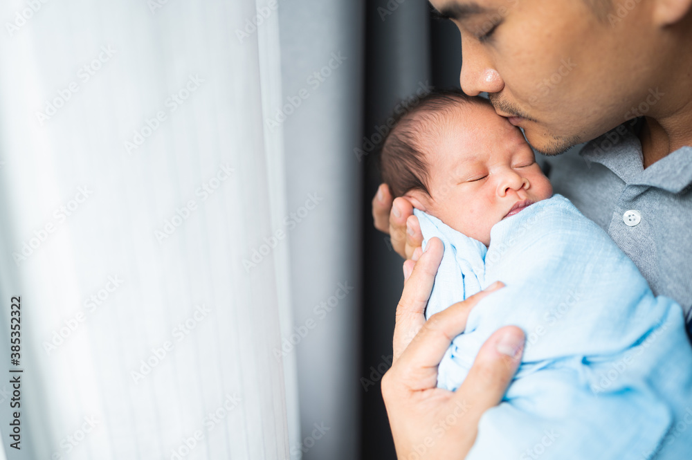 Portrait of young father kissing a newborn baby on his arm