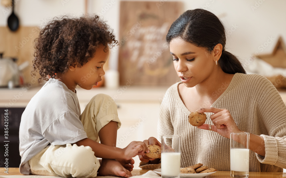 happy mulatto family mother and little son eat cookies with milk at home.