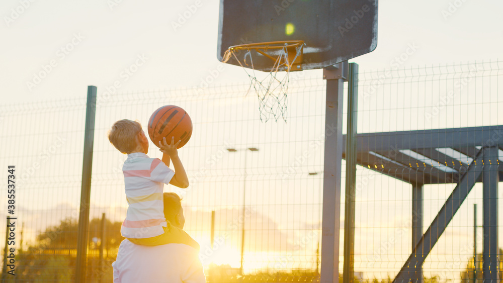 Father and son playing basketball at sunset