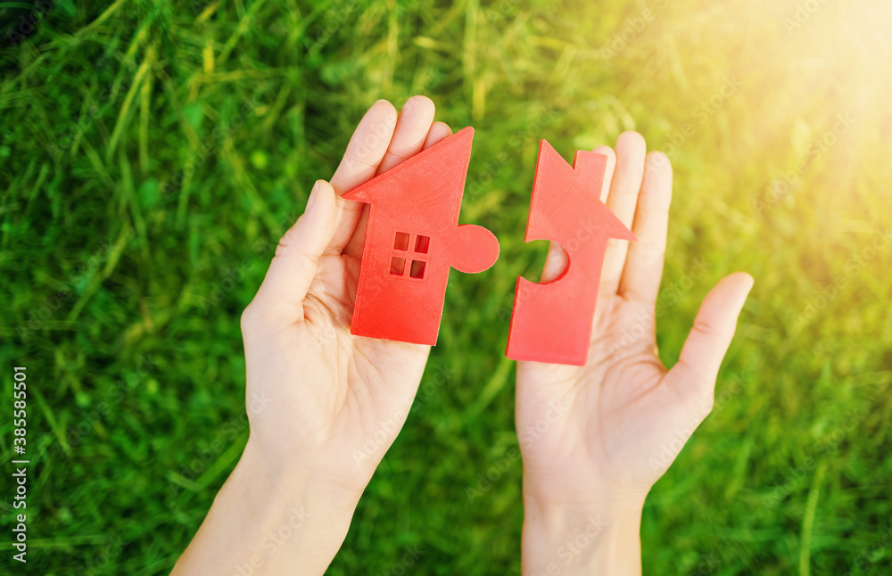 Red house with a shape of two parts of puzzle in human hands.