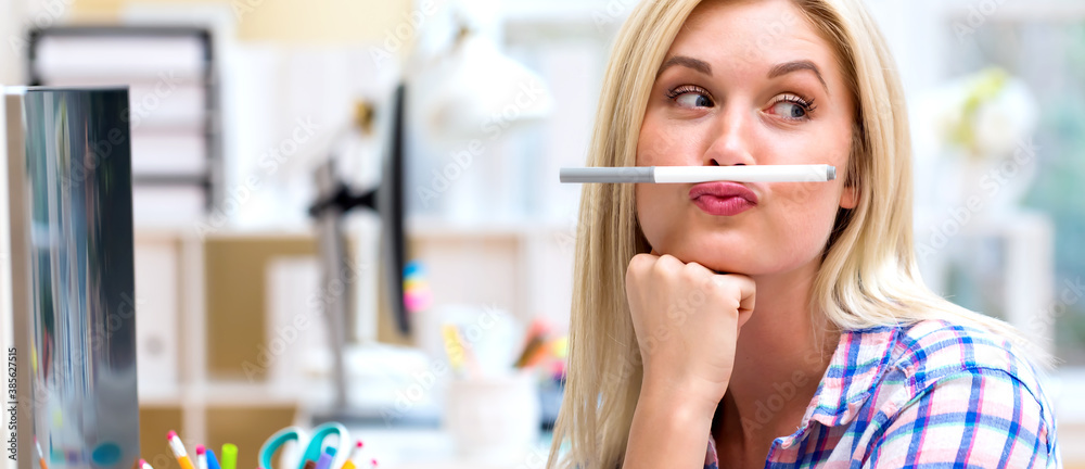 Young woman holding a pen above lips in an office