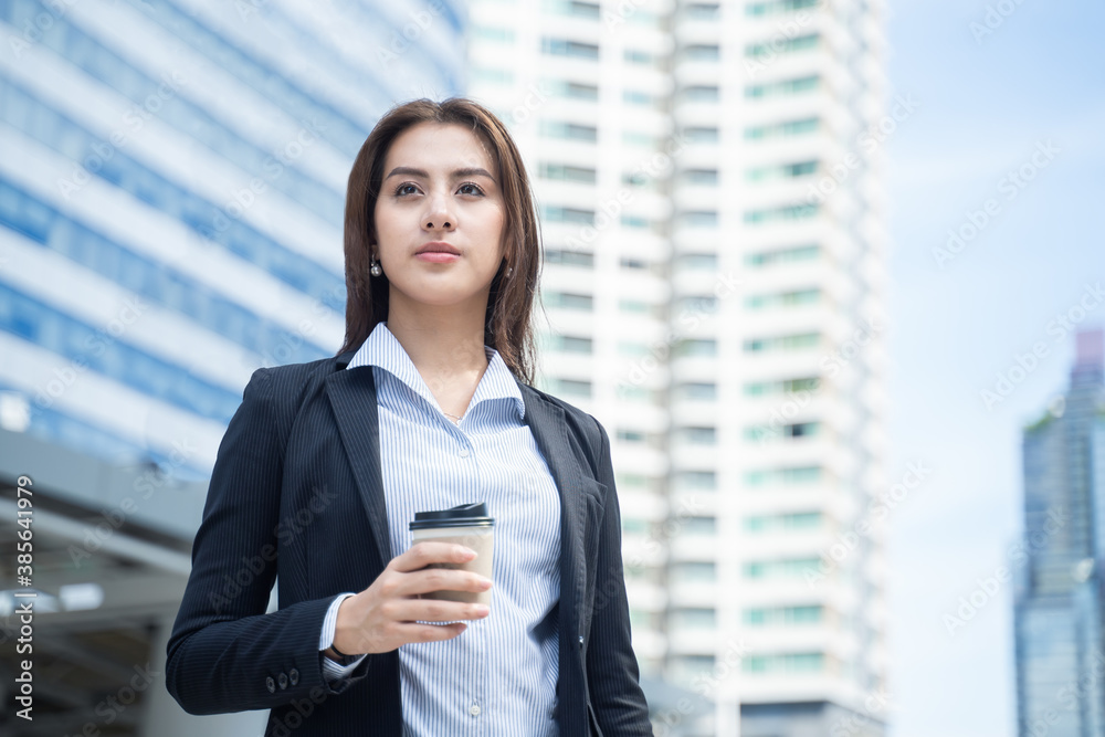 Asian young businesswoman drinking coffee and standing in the city.