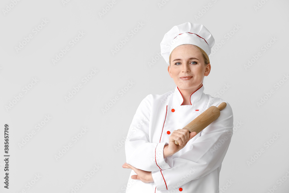 Mature female chef with rolling pin on grey background