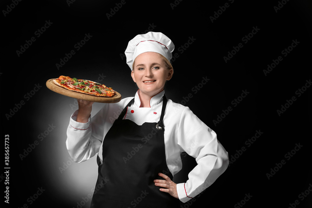 Mature female chef with tasty pizza on dark background