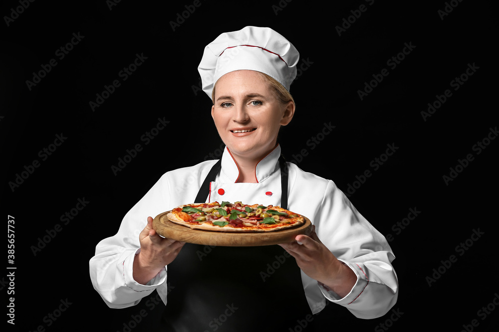 Mature female chef with tasty pizza on dark background