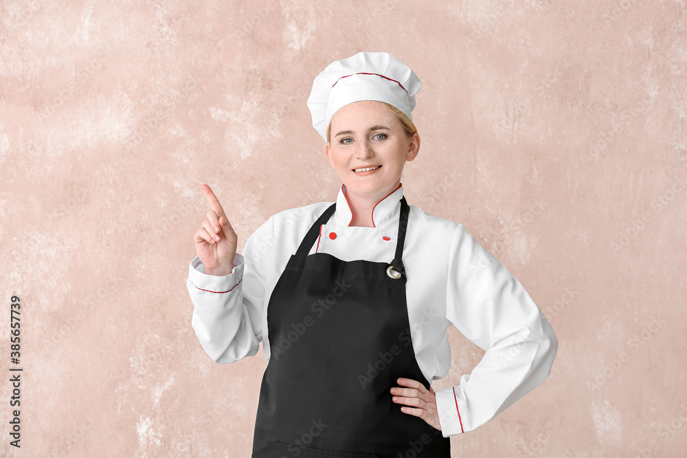 Mature female chef pointing at something on color background