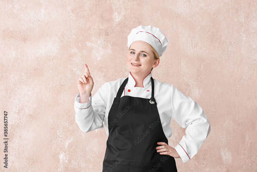 Mature female chef pointing at something on color background