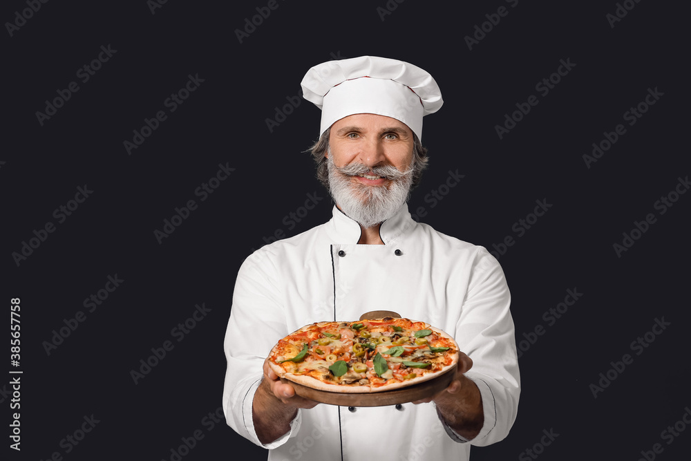 Mature male chef with tasty pizza on dark background