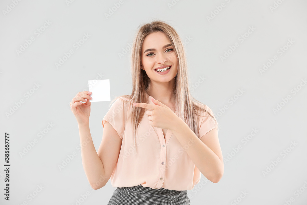 Young woman with small blank paper sheet on light background