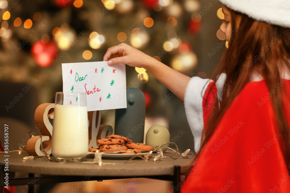 Little girl putting letter to Santa on table with treat